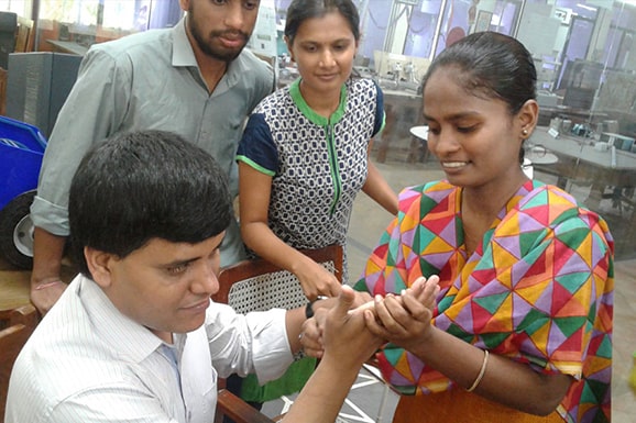 A lady writes on the palm of Pradip Sinha, member of Chetana’s advisory committee. Two people watch them communicate.