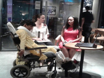 Two women talk to a man in a wheel chair, the three are sitting in an office