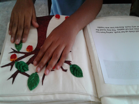 A young girl explores a page from an accessible tactile book – ‘Giving Tree’.